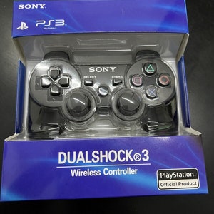 Può includere: Un controller wireless nero Sony DualShock 3 per PlayStation 3 nella sua confezione originale. Il controller presenta un design nero e grigio con pulsanti etichettati come Start, Select e PlayStation.