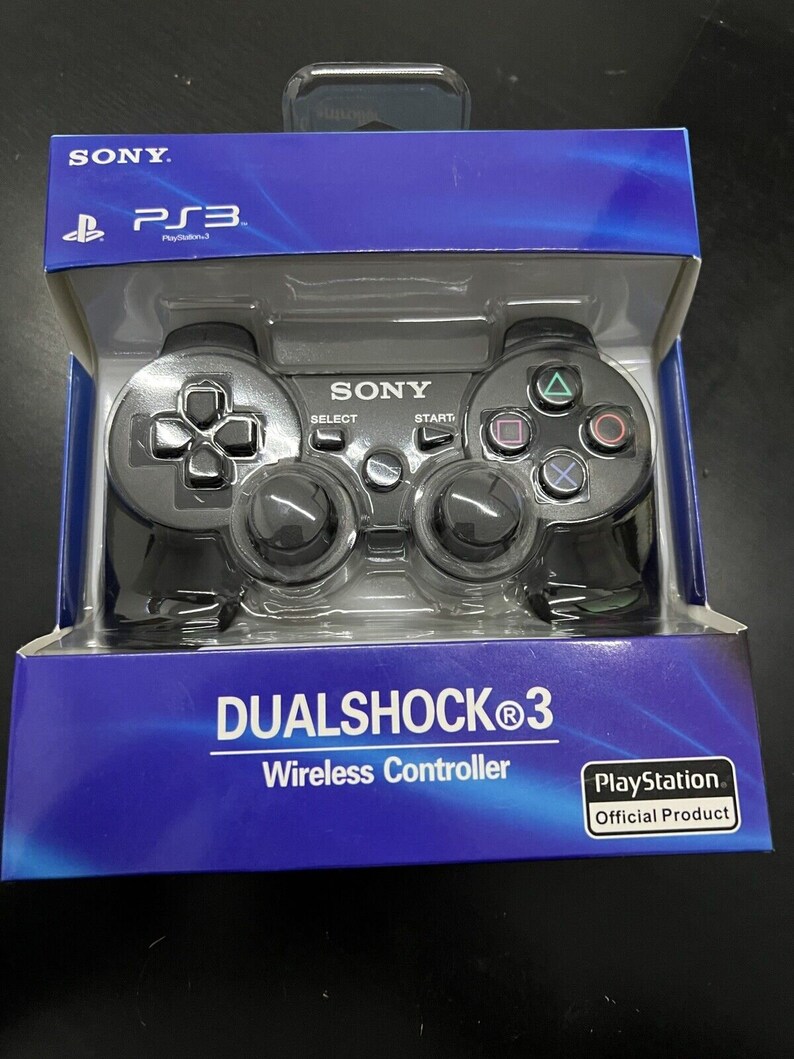 K&ouml;nnte beinhalten: Ein schwarzer Sony DualShock 3 Wireless-Controller f&uuml;r PlayStation 3 in seiner Originalverpackung. Der Controller hat ein schwarzes und graues Design mit Kn&ouml;pfen, die mit Start, Select und PlayStation beschriftet sind.