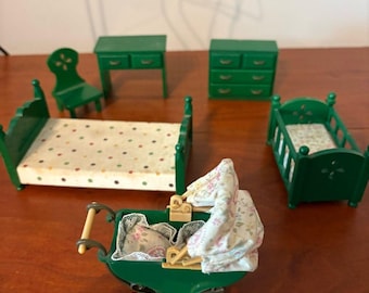 Op de afbeelding: Een miniatuur poppenhuismeubelset in donkergroen, inclusief een bed met een matras met stippen, een wieg, een bureau, een stoel, een ladekast en een groene kinderwagen met een kap met bloemenpatroon en beddengoed met kanten rand.