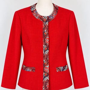 May include: A bright red long-sleeved jacket featuring a round neckline and a front button closure. The collar, front placket, and pocket flaps are accented with a multi-colored paisley pattern. The jacket includes five round red buttons.
