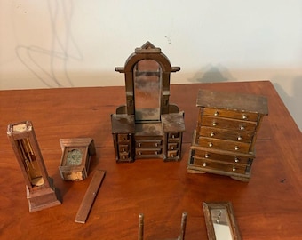 Op de afbeelding: Een verzameling miniatuur poppenhuismeubels van hout, waaronder een staande klok, een kleine klok, een kaptafel met spiegel, een ladekast, een rechthoekig houten stuk, een kleine standaard met twee verticale palen en een rechthoekige spiegel.