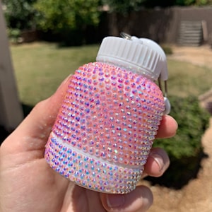May include: A white water bottle with a pink iridescent design covered in rhinestones.