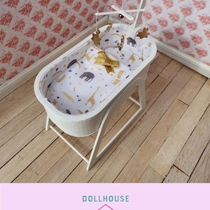 Può includere: Culla per bambole bianca con un materasso a motivi bianchi e dorati e un mobile con stelle dorate e animali appesi sopra.