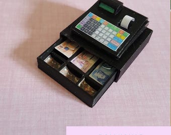 May include: A black cash register with a drawer that opens to reveal compartments for coins and bills. The cash register has a digital display and a keypad with colorful buttons.