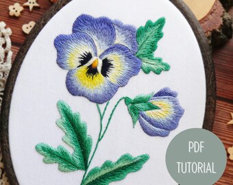 May include: Embroidered hoop art featuring a purple and yellow pansy flower with green leaves. The hoop is on a wooden surface with a text overlay that says "PDF TUTORIAL".