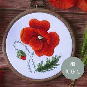 May include: Embroidered poppy flower in a wooden hoop with green leaves and a bud. The embroidery is on white fabric. The hoop is on a wooden surface with green grass.