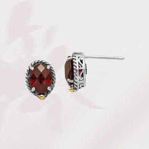 May include: A pair of silver earrings with a red gemstone set in a silver and gold filigree design.