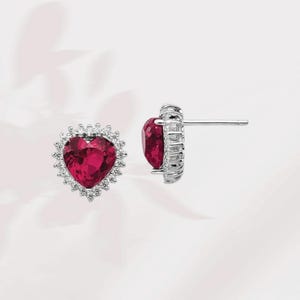 May include: A pair of heart-shaped earrings with a red gemstone surrounded by a halo of smaller white gemstones.