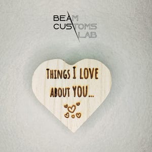 Pode incluir: Um sinal de madeira em forma de coração com o texto "Things I love about you..." e pequenos corações esculpidos na madeira.