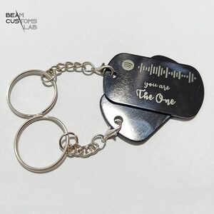 Pode incluir: Chaveiro de metal preto com dois anéis e uma corrente. O chaveiro tem uma etiqueta com um código de barras e o texto "you are The One".