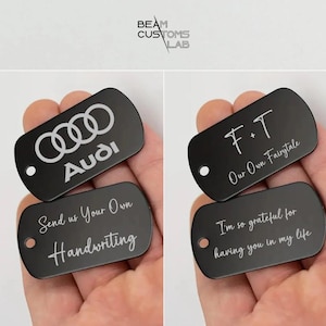 Pode incluir: Quatro etiquetas de cachorro de metal preto com texto gravado. A primeira etiqueta apresenta o logotipo da Audi e o texto "Audi". A segunda etiqueta tem o texto "Envie-nos sua própria caligrafia". A terceira etiqueta tem o texto "F+T Nosso próprio conto de fadas". A quarta etiqueta tem o texto "Sou tão grato por ter você na minha vida".