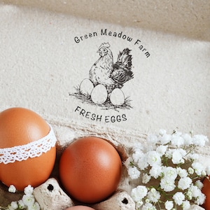 May include: A close-up of brown eggs, some with white lace trim, in a carton with white flowers. The image features a stamp with a hen, eggs, and the text "Green Meadow Farm FRESH EGGS."