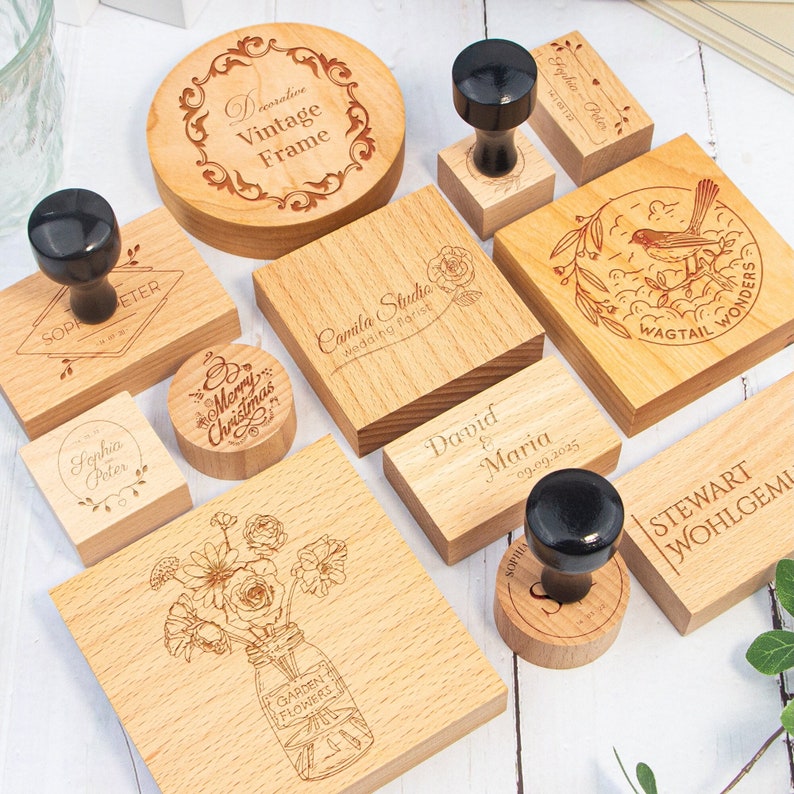 May include: A selection of wooden stamps featuring different designs, such as a decorative vintage frame, a floral bouquet, a bird with the text "Wagtail Wonders", a Christmas greeting, and a wedding announcement. The stamps are crafted from natural wood and have a rustic, handmade appearance.