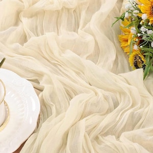 Könnte beinhalten: Eine weiße, durchsichtige Tischdecke aus Stoff mit zarter Textur. Der Stoff ist drapiert und gefaltet, wodurch weiche Falten und Wellen entstehen.