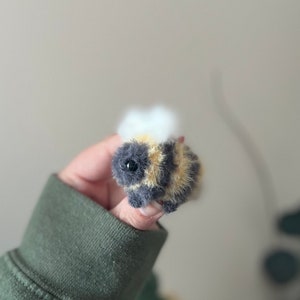 May include: A small, fuzzy, crocheted bee toy with black and yellow stripes and a white fuzzy head.
