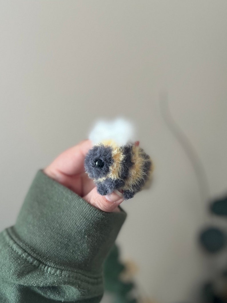 May include: A small, fuzzy, crocheted bee toy with black and yellow stripes and a white fuzzy head.