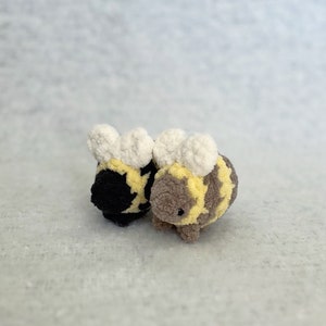 May include: Two plush bee toys, one black and one brown, with white fuzzy wings and yellow stripes.