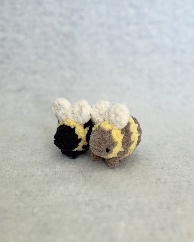 May include: Two plush bee toys, one black and one brown, with white fuzzy wings and yellow stripes.