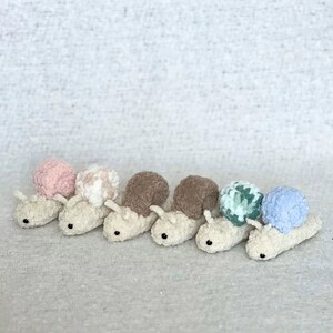 Puede incluir: Seis juguetes de caracol tejidos a crochet en fila. Los caracoles est&aacute;n hechos de hilo suave y esponjoso y tienen conchas de diferentes colores. Las conchas son rosa, blanca, marr&oacute;n, marr&oacute;n, verde y azul.