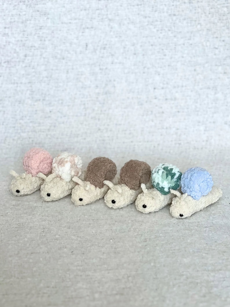 Puede incluir: Seis juguetes de caracol tejidos a crochet en fila. Los caracoles est&aacute;n hechos de hilo suave y esponjoso y tienen conchas de diferentes colores. Las conchas son rosa, blanca, marr&oacute;n, marr&oacute;n, verde y azul.