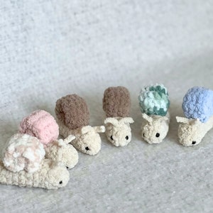 Puede incluir: Cinco juguetes de caracol de crochet en diferentes colores, incluyendo rosa, marr&oacute;n, verde, azul y blanco. Los caracoles est&aacute;n todos mirando en la misma direcci&oacute;n y tienen ojos negros.