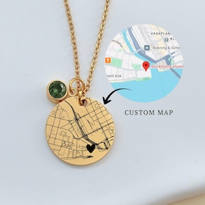 Può includere: Collana color oro con un ciondolo rotondo con un design di mappa personalizzato e una piccola gemma verde. Il ciondolo ha un cuore nero. Le parole "CUSTOM MAP" sono visibili.