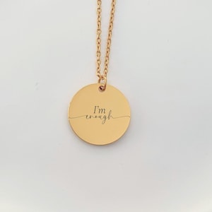 May include: Gold-coloured necklace featuring a circular pendant. The pendant is inscribed with the phrase "I'm enough" in a delicate, cursive font. The necklace is presented on a white, slightly curved surface.
