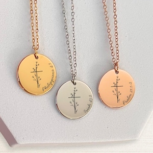 May include: Three round pendant necklaces in gold, silver, and rose gold. Each pendant features a cross design with floral accents and a Bible verse inscription. The necklaces hang on delicate chains.