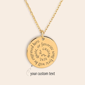 Può includere: Una collana con pendente dorato con un ciondolo circolare. Il ciondolo presenta un testo inciso sul bordo, con le parole "engraved here, or favorite song lyric, your custom text will be engraved". Il testo "your custom text" è anch'esso visibile.