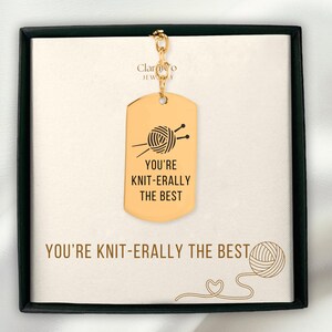May include: Gold-coloured dog tag pendant with a chain, featuring a yarn ball and knitting needles graphic. The tag reads "YOU'RE KNIT-ERALLY THE BEST". The pendant is displayed on a card with the same text and a yarn ball illustration.