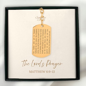 Peut inclure: Un pendentif en forme de plaque d'identification doré avec la prière du Seigneur gravée, suspendu à une chaîne dorée. La plaque est présentée sur une carte crème à l'intérieur d'une boîte noire. Le texte "The Lord's Prayer" et "Matthew 6:9-13" sont également visibles.
