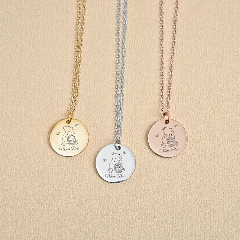 May include: Three gold, silver, and rose gold necklaces with a round pendant featuring a cartoon bear holding a honey pot. The pendant says "Mama Bear" on the bottom.