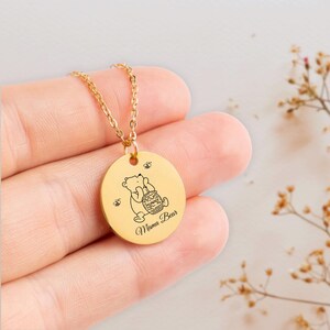 May include: Gold necklace with a round pendant featuring a cartoon bear holding a honey pot and the text "Mama Bear".