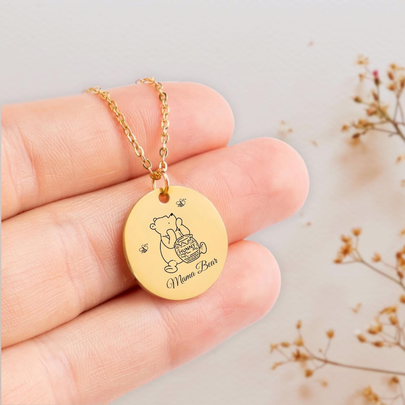 May include: Gold necklace with a round pendant featuring a cartoon bear holding a honey pot and the text "Mama Bear".