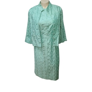 May include: A mint green dress and matching jacket set with a floral pattern. The dress has a fitted bodice and a skirt that falls to the knee. The jacket has a collar and three-quarter sleeves.