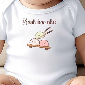 May include: A white baby onesie with the text "Banh bao nho" and a cartoon image of three steamed buns with chopsticks.