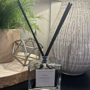 May include: A clear glass bottle with black reeds and a white label that reads "lemieux candle company white eucalyptus reed diffuser".