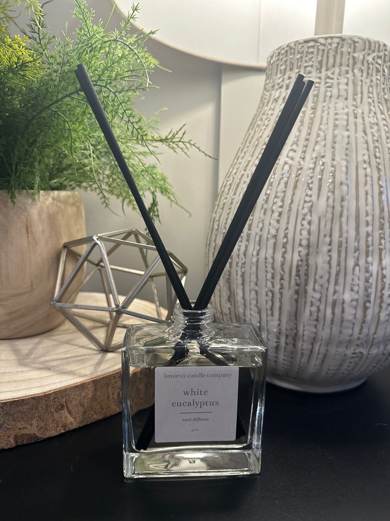 May include: A clear glass bottle with black reeds and a white label that reads "lemieux candle company white eucalyptus reed diffuser".