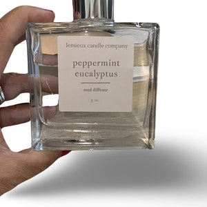 May include: A clear glass bottle with a silver cap and a white label that reads "lemieux candle company peppermint eucalyptus reed diffuser 5 oz."