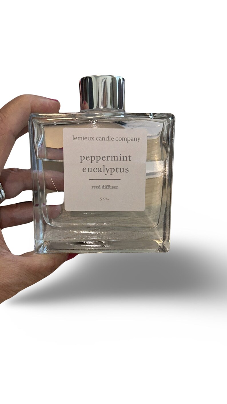 May include: A clear glass bottle with a silver cap and a white label that reads "lemieux candle company peppermint eucalyptus reed diffuser 5 oz."
