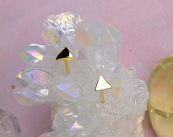 May include: Two gold triangle stud earrings with black tips, displayed on a white crystal cluster.