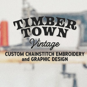 May include: Black and white logo for Timber Town Vintage, a business that offers custom chainstitch embroidery and graphic design. The logo is displayed on a wooden surface with a vintage sewing machine in the background.