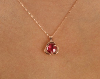 Op de afbeelding: Een delicate gouden ketting met een klein rood edelsteen hanger. De hanger is gevormd als een bloem met vier bloemblaadjes.
