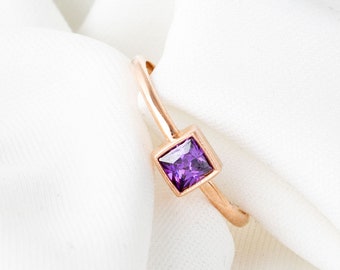 May include: A rose gold ring with a square-shaped purple gemstone.