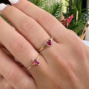 Può includere: Due anelli d'oro con pietre preziose rosse. Un anello presenta una pietra a forma di cuore, mentre l'altro anello ha una pietra rettangolare.