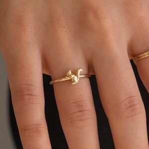 以下が含まれることがあります： 手には2つのゴールドリングが写っています。1つはリスのデザインで、もう1つは楕円形の白い宝石が付いています。リングは繊細で、金で作られているようです。