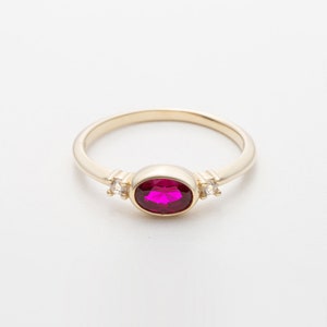 May include: A gold ring with a large oval-shaped ruby gemstone and two smaller round clear gemstones on either side.