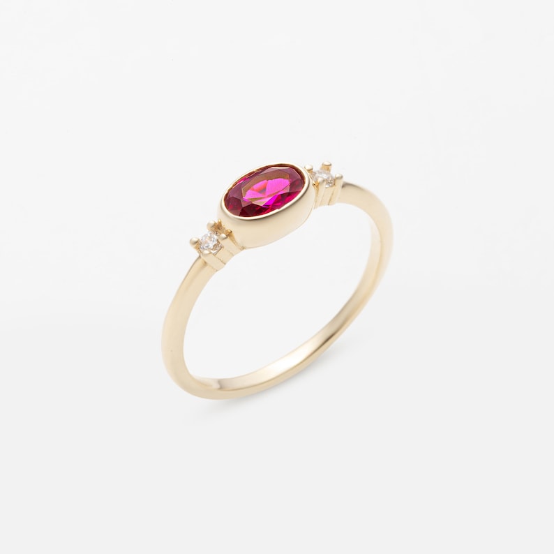 May include: A gold ring with a red oval gemstone and two smaller white gemstones on the band.
