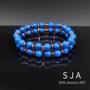 May include: A double-strand bracelet featuring vibrant blue beads and copper-colored metal accents. The beads are round and have a speckled appearance. The bracelet is displayed on a reflective black surface. The text "SJA SEM Jewelry ART" is visible.
