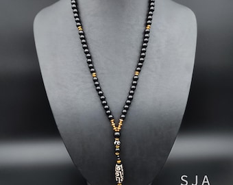 May include: A black beaded necklace with gold accents and a pendant featuring a geometric design. The necklace is displayed on a black mannequin. The pendant has a white background with black geometric shapes.